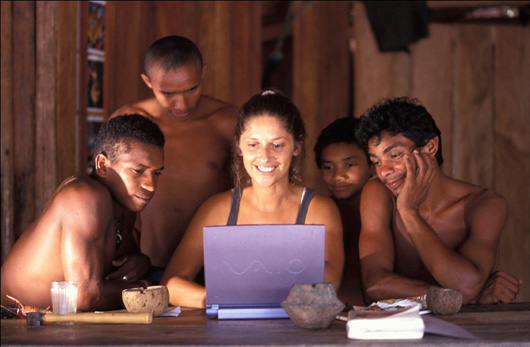 woman sitting at computer surrounded by male villagers
